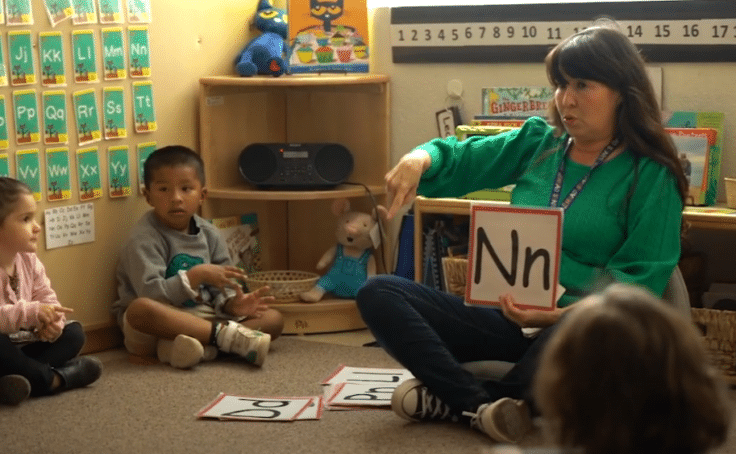 An early childhood educator holding a letter sign and talking to children