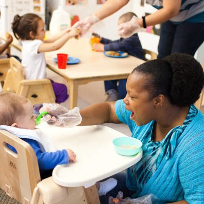 Child care teacher feeding infant in high chair