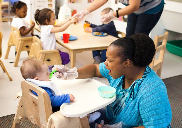 Child care teacher feeding infant in high chair