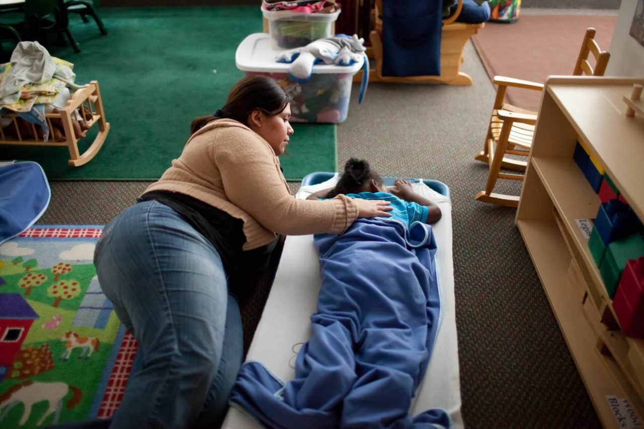 A child care educator lays on the floor with a child