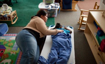 A child care educator lays on the floor with a child