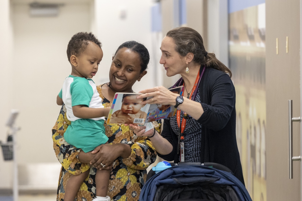 An early childhood professional showing a book to a mother and her toddler