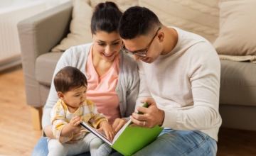 Latino parents read to toddler in mom's lap.
