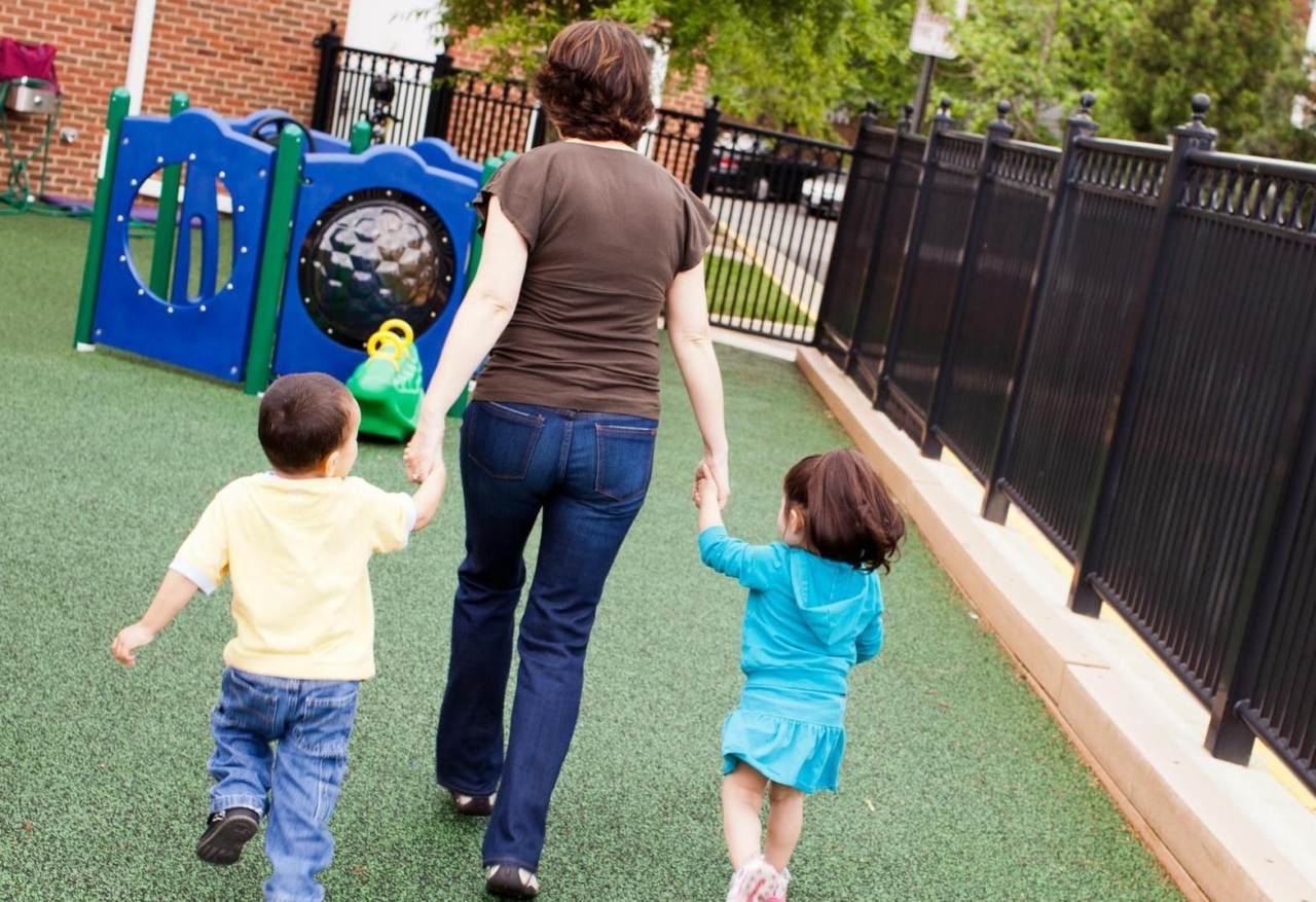 A child care professional holding hands and walking with two young children