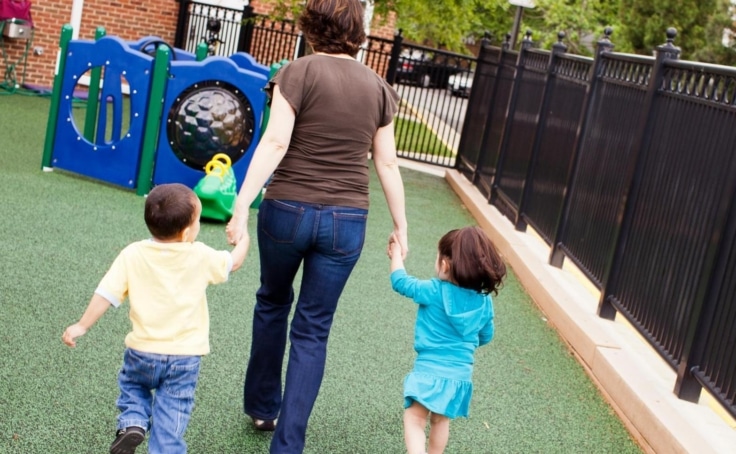 A child care professional holding hands and walking with two young children