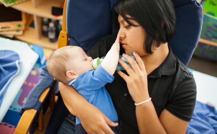 A child care worker holding an infant and feeding them with a bottle