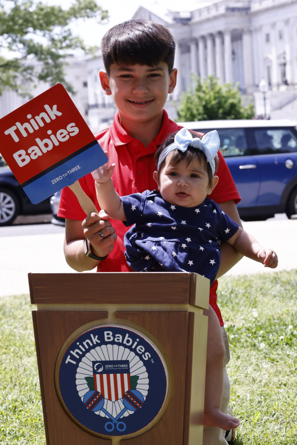 A young child holding an infant in front of the Capitol building in Washington, D.C.