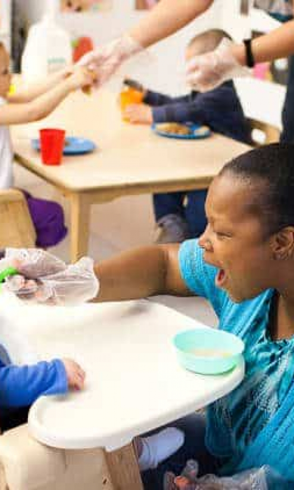 Child care teacher feeding infant in high chair